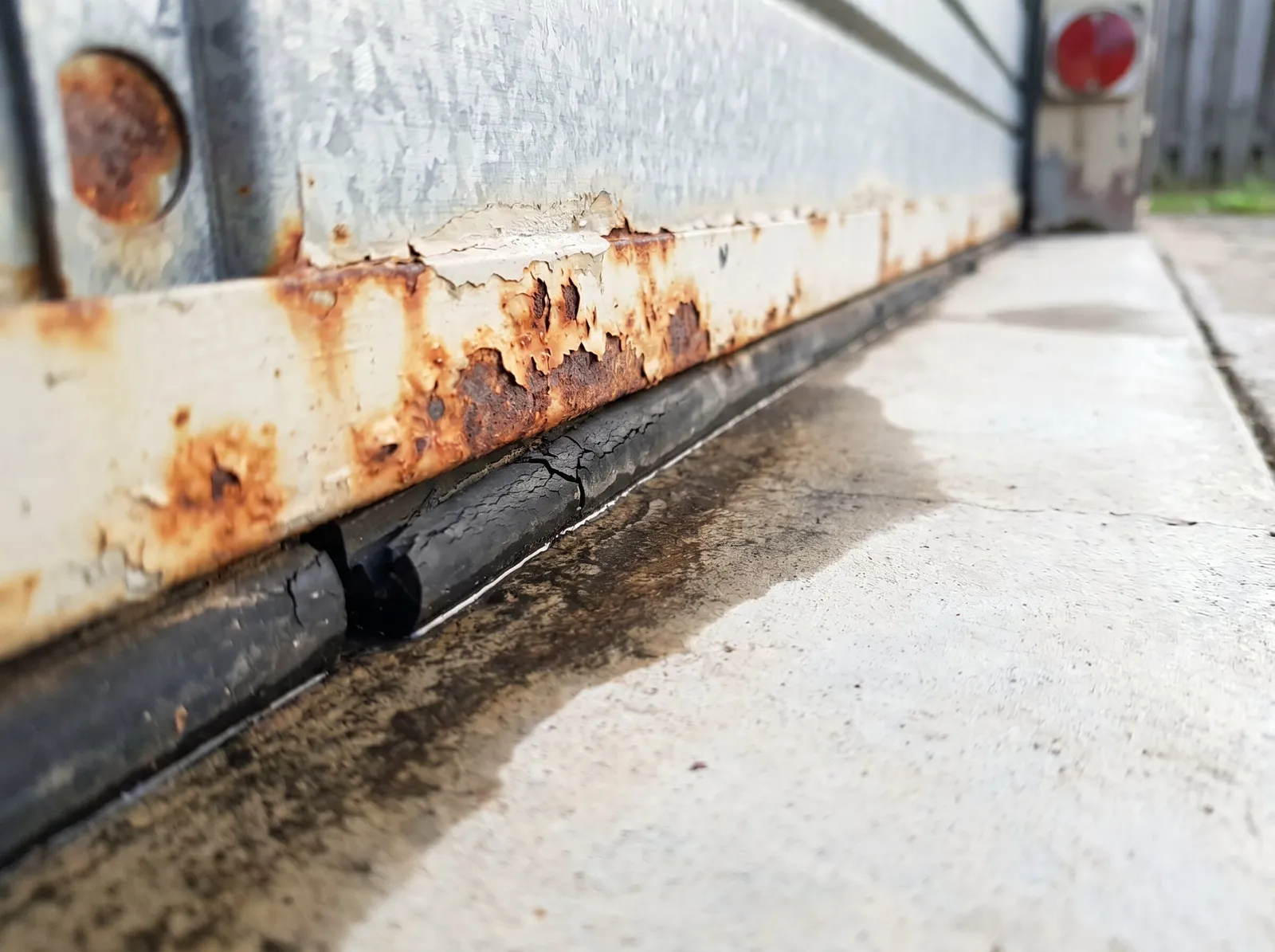 Rust blooming along the bottom rail of an ageing garage door above a cracked weather seal